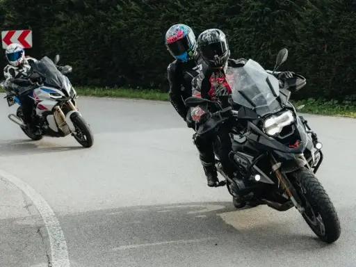 Motocykliści na zakręcie, jeden z pasażerem. Płynna zmiana biegów bez sprzęgła to klucz do dynamicznej jazdy.