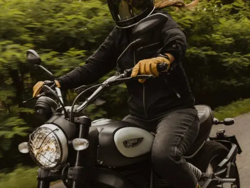 Motocyklista w kasku i żółtych rękawicach jedzie motocyklem. Zastanawia się, przy jakich obrotach zmieniać biegi, by jazda była płynna.