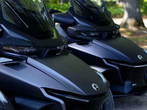 Dwa matowe, czarne pojazdy typu Can-Am Spyder stoją obok siebie na parkingu dla motocykli, gotowe do jazdy.