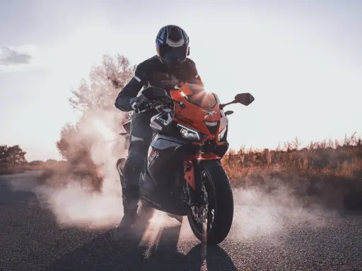 Motocyklista w kasku i kombinezonie na pomarańczowym Barton Blade 125, z którego unosi się dym. Zastanawiasz się, ile pali motor 125?