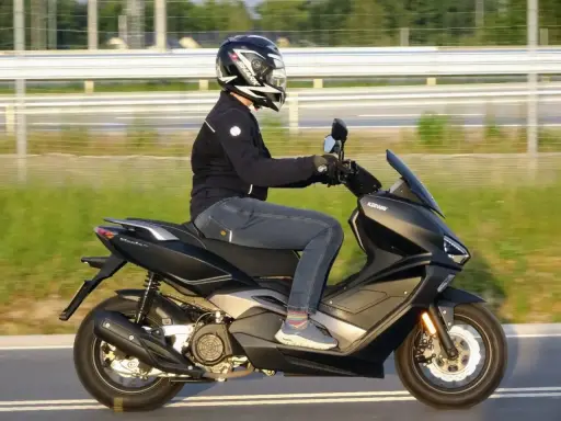 Pierwsze kroki w nauce jazdy na motorze 125. Kierowca w kasku i kurtce jedzie na skuterze Keeway po drodze.