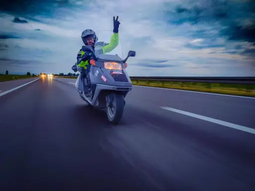 Motocyklista na skuterze 125 pozdrawia z autostrady, pokazując, że można nim jeździć po autostradzie.
