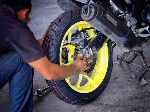 Mechanik dokonuje wymiany opon motocyklowych, pracując przy żółtej feldze i hamulcach.