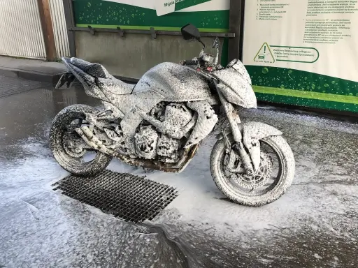 Motocykl pokryty pianą na myjni, gotowy do mycia. Instrukcja "jak myć motocykl" w tle.