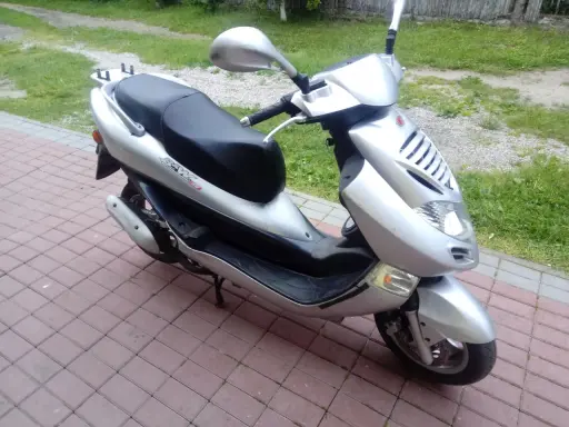 Srebrny skuter Kymco Bet&Win 50 stoi na chodniku z kostki brukowej.