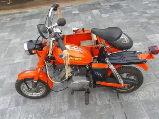 Pomarańczowa motorynka z koszem, ozdobiona płomieniami, gotowa na przejażdżkę.