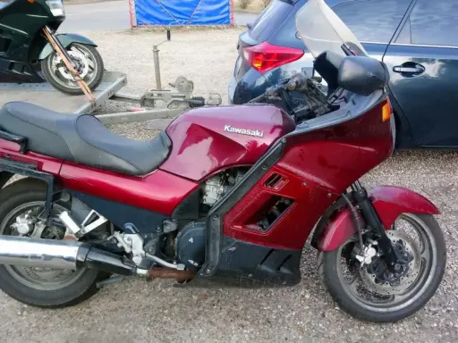 Czerwony motocykl Kawasaki GTR 1000 na przyczepce, obok ciemny samochód.