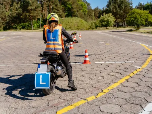 Nauka jazdy motocyklem na placu manewrowym. Osoba w kamizelce odblaskowej z literą "L" na motocyklu.