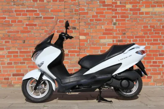 Biały skuter Suzuki Burgman 650 na tle ceglanej ściany. Zastanawiasz się nad jego spalaniem?