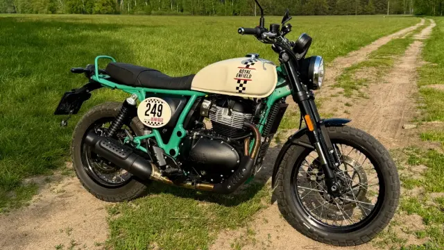 Zielony Royal Enfield Scrambler z numerem 249 na tle łąki i lasu. Gotowy na przygodę!