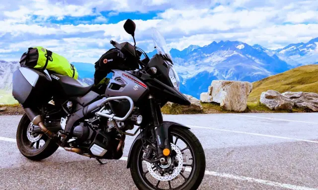 Szary motocykl Suzuki V-Strom, idealny motocykl do turystyki we dwoje, zaparkowany na tle majestatycznych gór i błękitnego nieba.