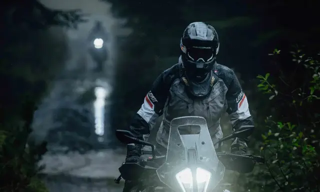 Motocyklista w kasku i kurtce Leatt przemierza leśną drogę w deszczu. Jazda na motocyklu w trudnych warunkach.