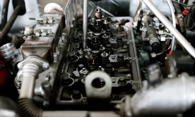 Wnętrze silnika z widocznymi zaworami i wtryskiwaczami. Mechanik sprawdza, czy nie występuje co to jest spalanie stukowe, które może uszkodzić jednostkę.