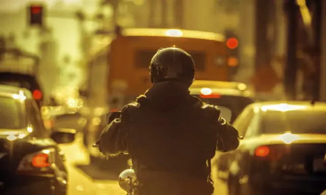 Motocyklista w kasku i kurtce w korku miejskim. Czy motor może jechać między samochodami? Tak, ten motocyklista próbuje.