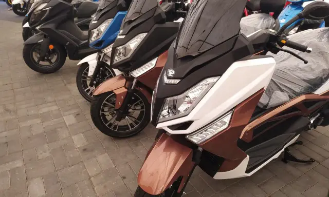 Kilka skuterów, w tym brązowy zipp qr max 125, stoi na chodniku.
