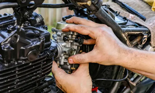 Dłonie mechanika regulują gaźnik motocykla, gdy ssanie jest włączone.