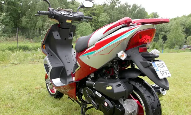 Czerwony skuter 50cc na trawie. Zastanawiasz się, ile jedzie skuter 50 bez blokad? Ten model wygląda na gotowy do szybkiej jazdy!