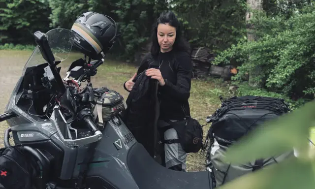 Kobieta pakuje plecak na motocykl. Zastanawia się, co zabrać na wyprawę motocyklową, by niczego nie zapomnieć.