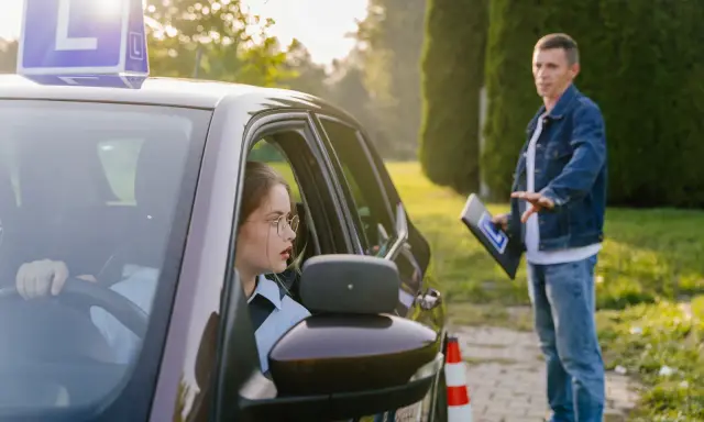 Młoda kobieta w okularach uczy się jeździć, a instruktor pokazuje jej, ile ważny jest kurs prawa jazdy.