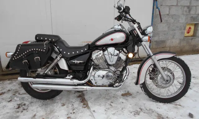 Czarny motocykl Zipp Roadstar 250 z sakwami, błyszczącymi chromami i ozdobnymi nitami, stoi na zaśnieżonym podjeździe.