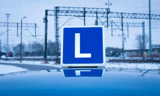 Tablica z literą "L" na dachu samochodu, symbolizująca naukę jazdy i teorię na prawo jazdy. W tle zimowy krajobraz z torami kolejowymi.