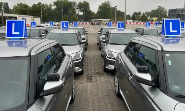 Rząd srebrnych aut z niebieskimi literami "L" na dachach. Czekają na kursantów, którzy zdali teorię i chcą jak najszybciej zdać praktykę.