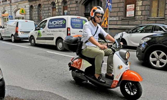 Mężczyzna w kasku jedzie skuterem elektrycznym, przygotowując się do testu na kartę motorowerową.