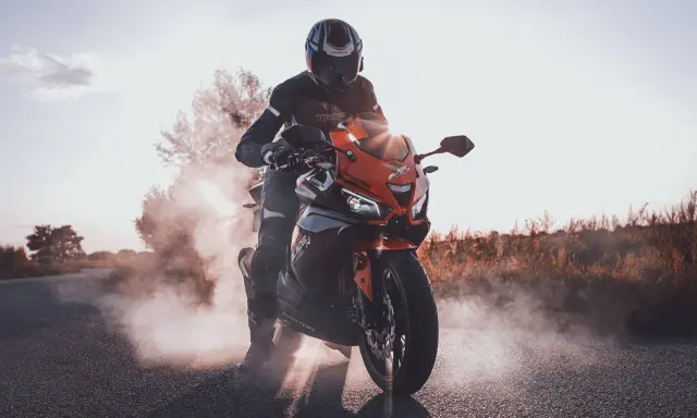 Motocyklista w kasku i kombinezonie na pomarańczowym Barton Blade 125, z którego unosi się dym. Zastanawiasz się, ile pali motor 125?