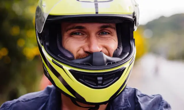 Uśmiechnięty mężczyzna w żółtym kasku motocyklowym. Dobór odpowiednich rozmiarów kasków motocyklowych to klucz do bezpieczeństwa.
