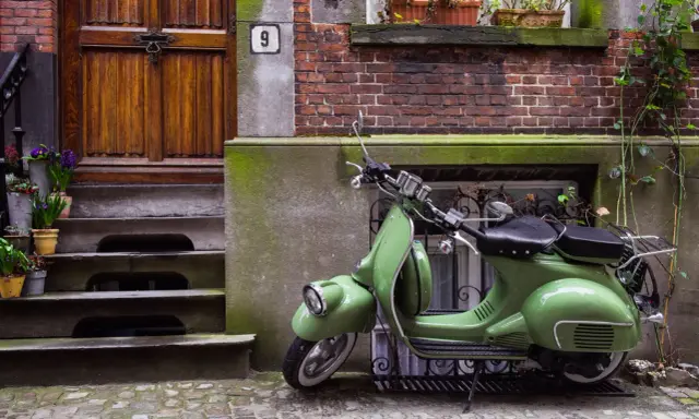 Zielony skuter, klasyk, czeka na właściciela. Parkowanie motocykla na chodniku przed drzwiami z numerem 9.