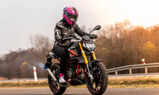 Motocyklistka w kolorowym kasku pędzi na czarnym motocyklu. Zastanawiasz się, ile waży litr benzyny, gdy tankujesz przed podróżą?