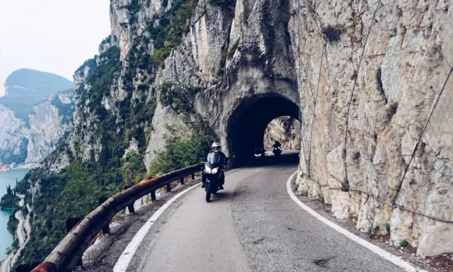 Motocykliści przemierzają malowniczą strada della forra, wjeżdżając w skalny tunel. Widok na jezioro i góry zapiera dech.