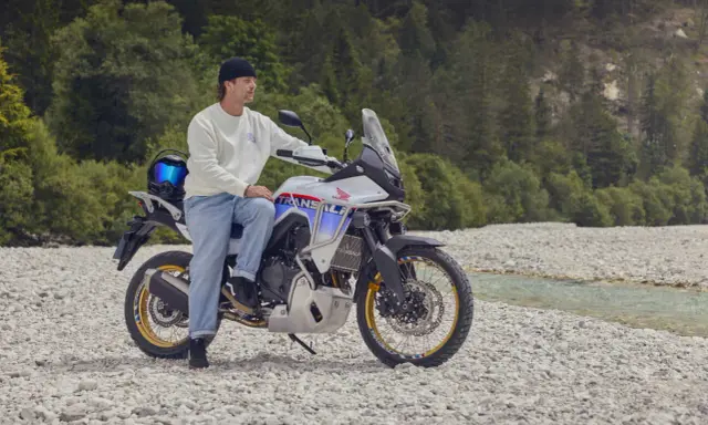 Mężczyzna na motocyklu Honda Transalp, gotowy na przygodę motocyklem po Europie. W tle las i strumień.