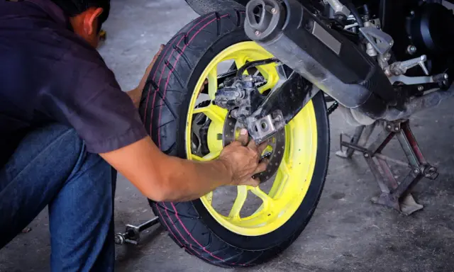Mechanik dokonuje wymiany opon motocyklowych, pracując przy żółtej feldze i hamulcach.
