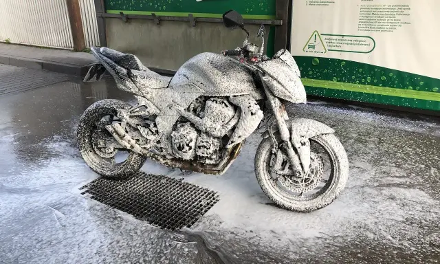 Motocykl pokryty pianą na myjni, gotowy do mycia. Instrukcja "jak myć motocykl" w tle.