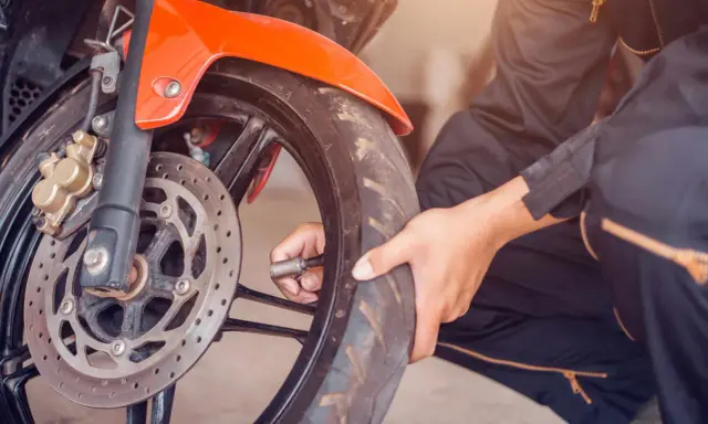 Sprawdzanie, jakie ciśnienie w oponach motocyklowych jest kluczowe dla bezpieczeństwa. Dłoń z manometrem przy wentylu przedniego koła.