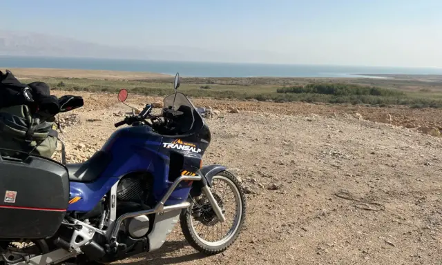Motocykl Honda Transalp z bagażami gotowy do podróży, z widokiem na Morze Martwe. Dokumenty, jak **carnet de passage**, czekają na przygodę.
