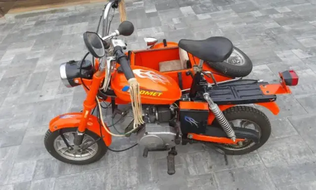 Pomarańczowa motorynka z koszem, ozdobiona płomieniami, gotowa na przejażdżkę.