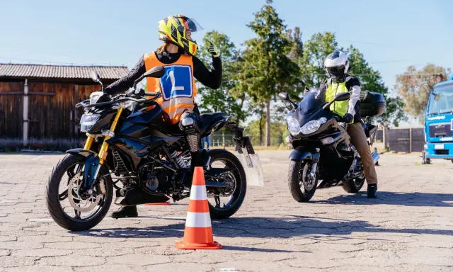 Nauka jazdy na motocyklu. Kursant w kamizelce z literą "L" i kasku na motocyklu, gotowy do zdobycia prawko na motocykl.