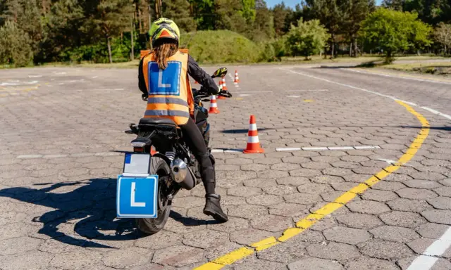 Nauka jazdy motocyklem na placu manewrowym. Osoba w kamizelce odblaskowej z literą "L" na motocyklu.