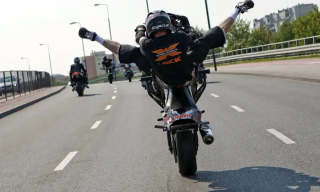 Motocyklista wykonuje jazdę na jednym kole z nogami w powietrzu. Ryzykowne wyczyny mogą skończyć się mandatem.