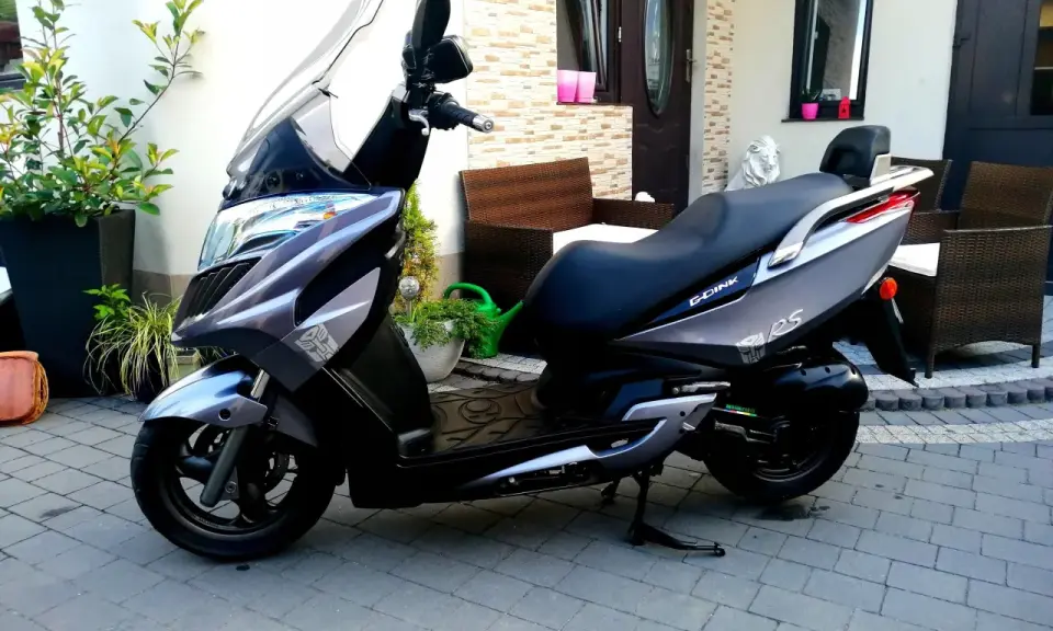 Elegancki skuter Kymco Dink 50 w kolorze grafitowym stoi na podjeździe, gotowy do jazdy.
