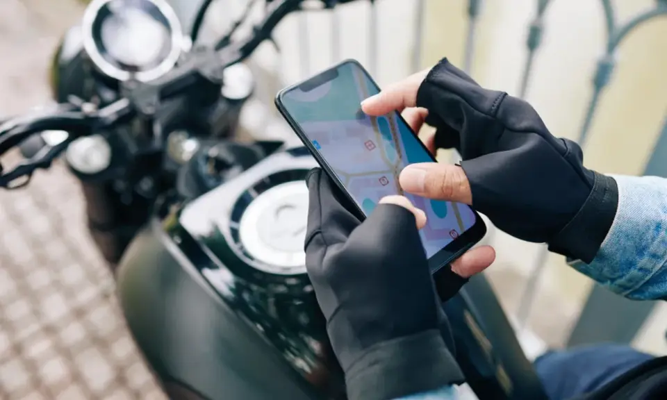 Motocyklista w rękawiczkach sprawdza trasę na mapie w aplikacji dla motocyklistów.