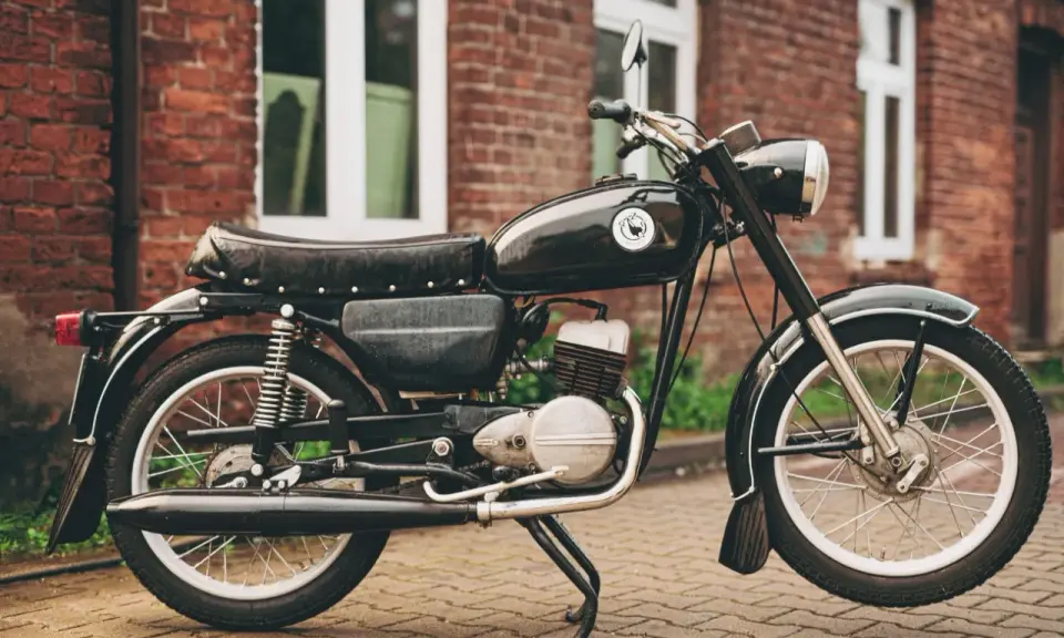 Czarny motocykl wsk 125 na tle ceglanego budynku. Klasyk z PRL-u gotowy do jazdy.