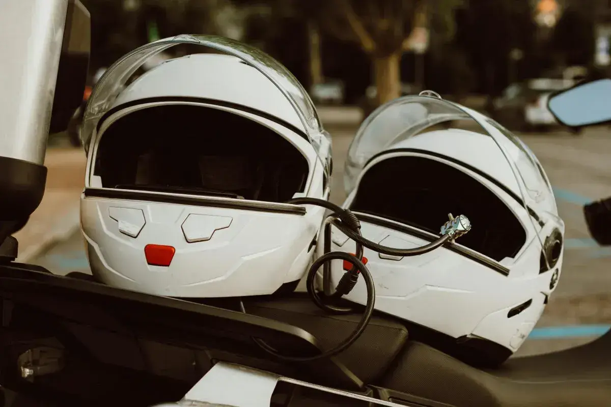 Dwa białe kaski motocyklowe połączone blokadą. Gotowe do podróży, czekają na właścicieli.