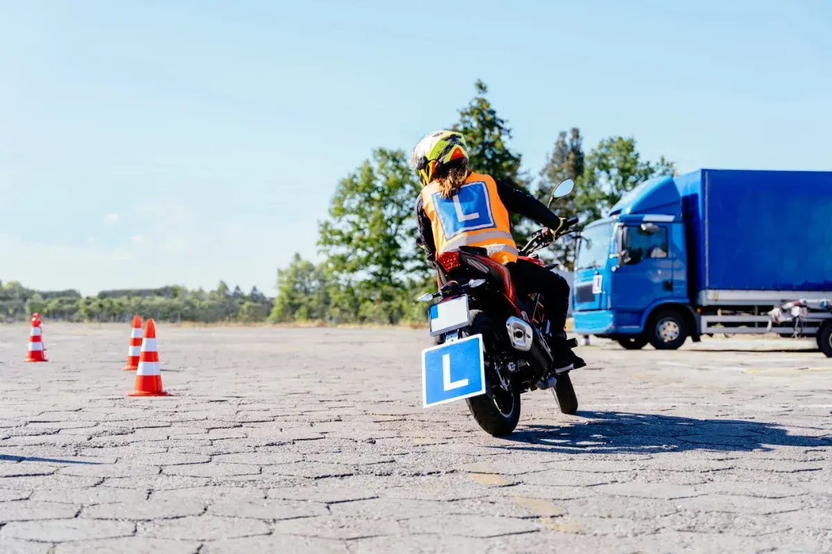 Osoba na motocyklu z literą "L" na kamizelce i tablicy, ćwiczy jazdę. Mam prawo jazdy B, chcę zrobić A.