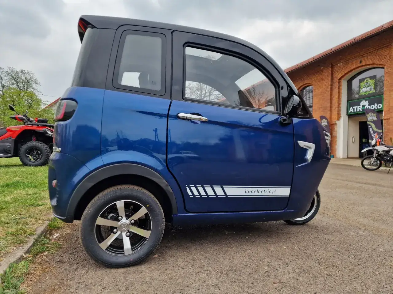 Niebieski, zabudowany skuter elektryczny, idealny do miasta, nie wymaga prawa jazdy. Obok quad i motocykl.