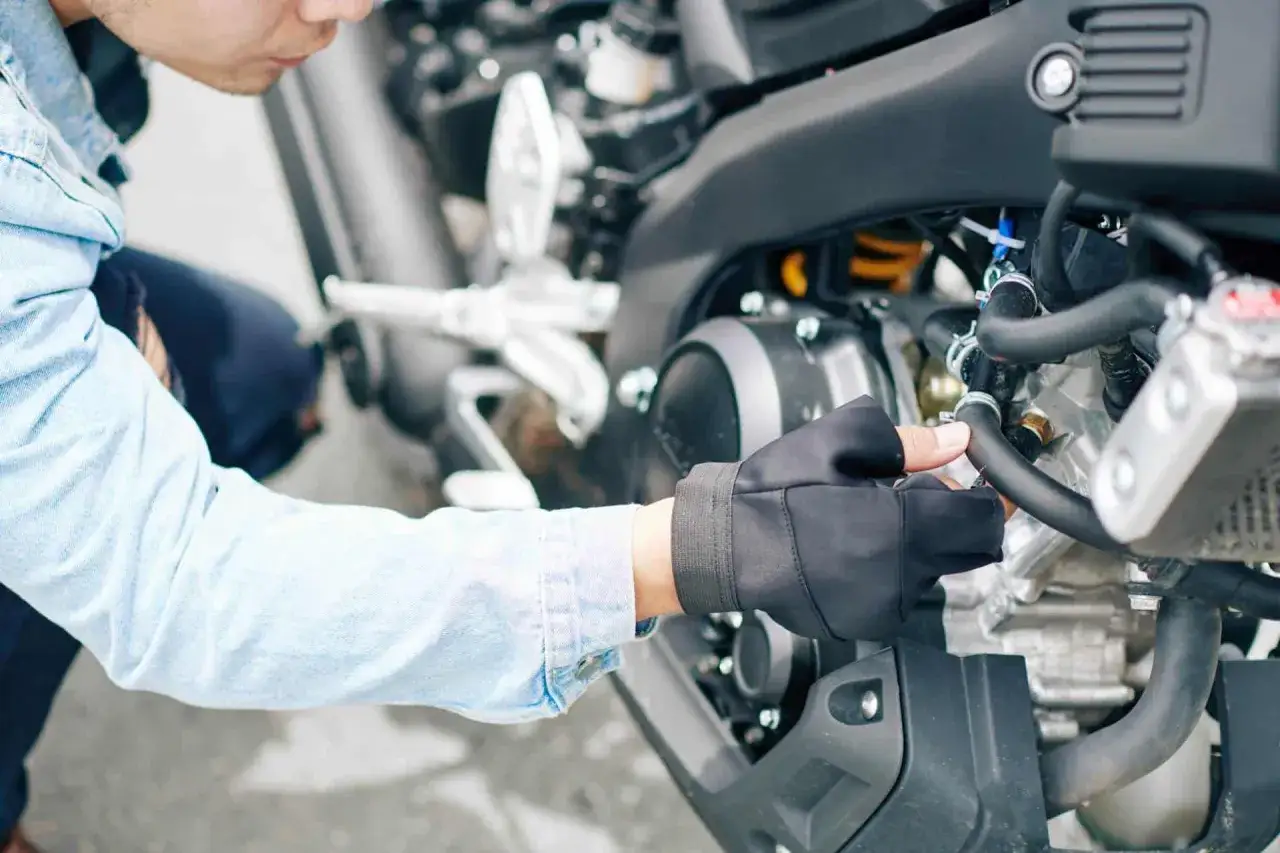 Mężczyzna w rękawiczce dokonuje wymiany oleju w motocyklu, dbając o jego sprawne działanie.