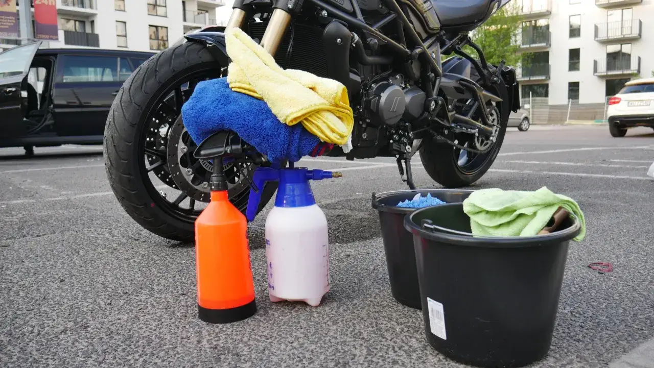 Przygotowania do mycia motocykla: dwa wiadra, butelki z płynem i ściereczki czekają na rozpoczęcie pracy.