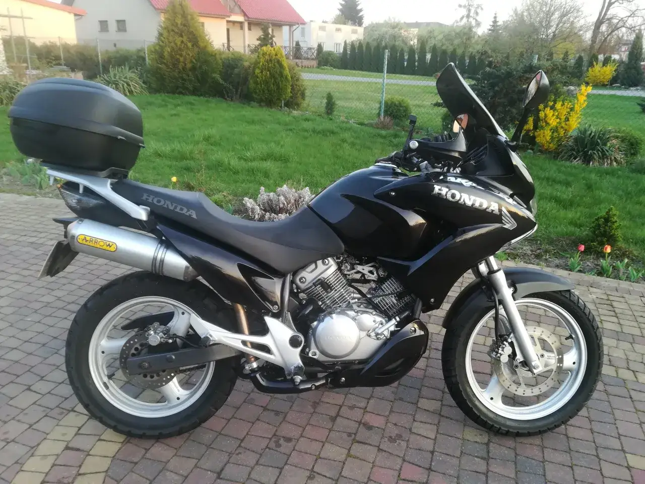 Czarny motocykl Honda Varadero 125 z kufrem i wydechem Arrow. Gotowy na odblokowanie mocy i przygodę!